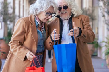 Kafkasyalı mutlu çift dışarıda alışveriş gününün tadını çıkarıyor. Renkli alışveriş torbaları tutarken, şık ceketler giyerken gülümserler. Yaşam tarzı, aşk, eğlence ve bağlantı kavramı. 