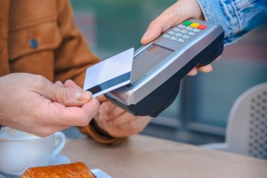 POS terminali olan bir kafe masasında temas kurulamayan iki kişinin yakın çekimi. Kahve ve pasta görülebilir. Kentsel ortamlarda modern yaşam tarzı ve dijital finans kavramı. 