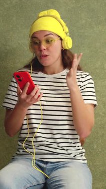 Çizgili tişörtlü beyaz kadın akıllı telefona bakarken heyecanla yumruğunu kaldırıyor. Bir galibiyeti kutluyor, muhtemelen online bir bahisten. Yeşil duvarlı ve dikey dikey dikey dikey dekorlu parlak bir sahne.