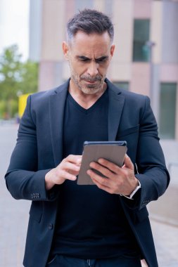 Kendine güvenen bir işadamı modern bir şehir ortamında tablet kullanıyor. Odaklanmış ve profesyonel görünüyor. Dijital iş, teknoloji ve çağdaş iş hayatı kavramı. Dikey