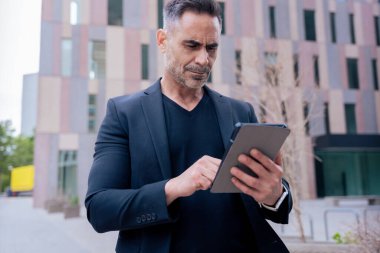 Kendine güvenen bir işadamı modern bir şehir ortamında tablet kullanıyor. Odaklanmış ve profesyonel görünüyor. Dijital iş, teknoloji ve çağdaş iş hayatı kavramı. 
