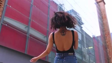 Afro-Amerikalı bir kadın şehir ortamında banklar arasında yaratıcı bir pozda dans ediyor. Günlük kıyafetler giyiyor ve denge, güç ve ifade gösteriyor. Hareket, sanat ve özgürlük kavramı