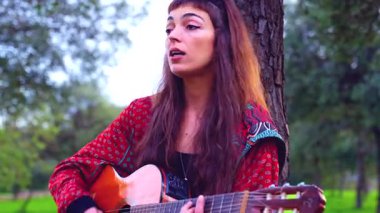 Genç bayan müzisyen, sakin bir açık hava parkında akustik gitarla şarkı söylüyor. Doğa tarafından çevrelenmiş, tutku, yaratıcılık ve duyguyu gündelik bir ortamda müzik yoluyla ifade eder.. 
