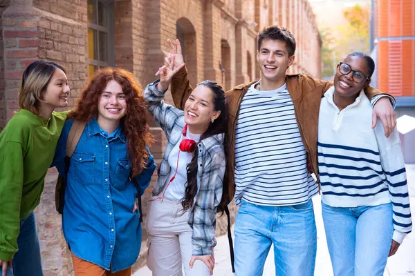 Çok ırklı bir grup öğrenci üniversitede yürüyor, dışarıda gülüyor. Gençler birlikte eğleniyor..