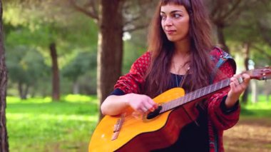 Genç bayan müzisyen, sakin bir açık hava parkında akustik gitarla şarkı söylüyor. Doğa tarafından çevrelenmiş, tutku, yaratıcılık ve duyguyu gündelik bir ortamda müzik yoluyla ifade eder.. 