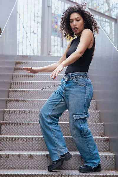 Afro-Amerikalı bir kadın şehir ortamında banklar arasında yaratıcı bir pozda dans ediyor. Günlük kıyafetler giyiyor ve denge, güç ve ifade gösteriyor. Hareket, sanat ve özgürlük kavramı. Dikey