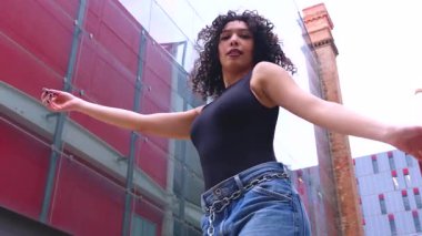 Afro-Amerikalı bir kadın şehir ortamında banklar arasında yaratıcı bir pozda dans ediyor. Günlük kıyafetler giyiyor ve denge, güç ve ifade gösteriyor. Hareket, sanat ve özgürlük kavramı