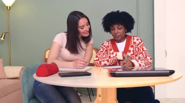 Afro-Amerikalı ve beyaz kadınlar bir masada oturup defterlere yazı yazıyorlar. Gülümser ve birlikte çalışırlar. Kapalı bir ortamda öğrenme, arkadaşlık, çeşitlilik ve eğitim kavramı. 