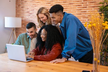 Çeşitli genç arkadaşlar bir dizüstü bilgisayarın etrafında toplandılar. Sırıtarak ve etkileşerek, tuğla duvar, teknoloji ve dostluğu simgeleyen, samimi bir iç mekanda, ahşap bir masada oturuyorlardı.. 