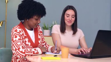 Kafkas ve Afrikalı Amerikalı öğrenciler dizüstü bilgisayar ve defter kullanarak birlikte çalışırlar. Odaklanmış ve neşeliler, öğrenme, çeşitlilik ve takım çalışmasını temsil eden kapalı bir alanda işbirliği yapıyorlar.. 