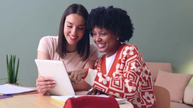 Mutlu Afrikalı Amerikalı ve Kafkasyalı öğrenciler birlikte oturup tablete bakıyorlar. Modern ortamlarda arkadaşlık, teknoloji ve öğrenme. Sosyal medyanın, eğitimin ve dijital bağlantının keyfini çıkarıyorlar.