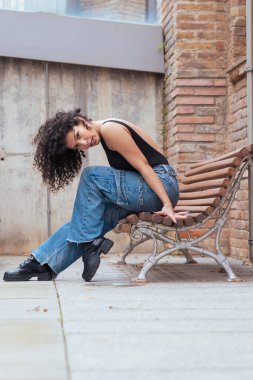 Afro-Amerikalı bir kadın şehir ortamında banklar arasında yaratıcı bir pozda dans ediyor. Günlük kıyafetler giyiyor ve denge, güç ve ifade gösteriyor. Hareket, sanat ve özgürlük kavramı. Dikey