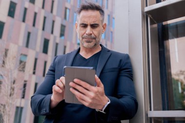 Kendine güvenen bir işadamı modern bir şehir ortamında tablet kullanıyor. Odaklanmış ve profesyonel görünüyor. Dijital iş, teknoloji ve çağdaş iş hayatı kavramı. 