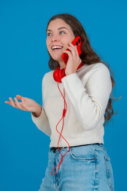 Kırmızı bir akıllı telefondan konuşan neşeli genç bir kadının dikey görüntüsü. Elini göğsüne koyup gülüyor. Parlak mavi bir arka plana yaslanıyor. Sıradan bir anda.. 