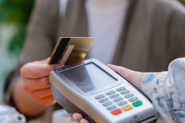 Bir POS terminalinde kredi kartıyla temas kurulamayan bir kişinin yakın plan görüntüsü. Sahne, arka planında çaydanlık olan bir kafe ortamında geçiyor. Modern işlem kolaylığını gösteriyor. 