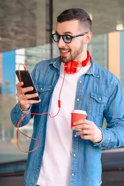 Şehir ortamında akıllı telefonunu kullanırken kırmızı kulaklıklı genç adam kahvenin tadını çıkarıyor. O okurken ya da mesajlaşırken gülümsüyor, modern cam binaların önünde sıradan bir anda duruyor. Dikey