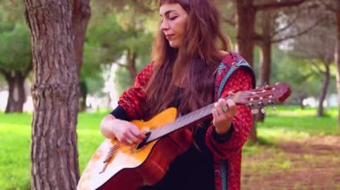 Genç bayan müzisyen, sakin bir açık hava parkında akustik gitarla şarkı söylüyor. Doğa tarafından çevrelenmiş, tutku, yaratıcılık ve duyguyu gündelik bir ortamda müzik yoluyla ifade eder.. 