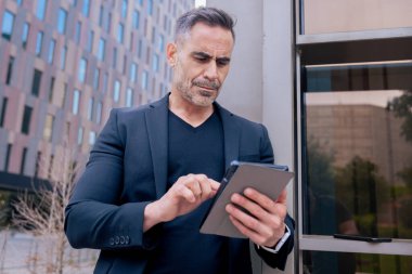 Kendine güvenen bir işadamı modern bir şehir ortamında tablet kullanıyor. Odaklanmış ve profesyonel görünüyor. Dijital iş, teknoloji ve çağdaş iş hayatı kavramı. 
