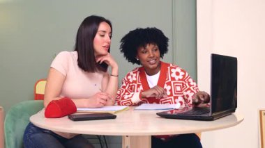 Kafkas ve Afro-Amerikalı öğrenciler dizüstü bilgisayar ve not defteri kullanarak birlikte çalışırlar. Odaklanmış ve neşeli bir şekilde, öğrenme, çeşitlilik ve takım çalışmasını temsil eden, kapalı bir alanda işbirliği yaparlar. Dikey