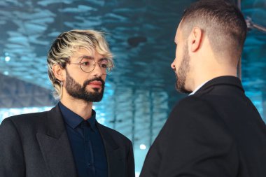 Takım elbiseli iki erkek profesyonel şık cam bir ofiste ciddi bir konuşma yapıyorlar. Çağdaş bir iç mekanda iş tartışması, kurumsal planlama veya müzakere. 