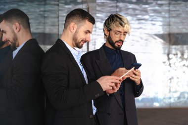 Takım elbiseli iki genç işadamı, modern, şık bir ofis alanında yansıtıcı cam duvarlar ve profesyonel, teknoloji odaklı bir atmosferle işbirliği yaparken dijital tabletlere odaklandılar.. 