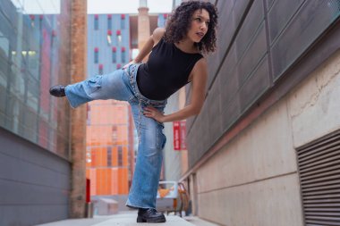Afro-Amerikalı bir kadın şehir ortamında banklar arasında yaratıcı bir pozda dans ediyor. Günlük kıyafetler giyiyor ve denge, güç ve ifade gösteriyor. Hareket, sanat ve özgürlük kavramı