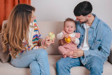 Gülümseyen ebeveynler kanepede otururken oyuncak tutan kızlarıyla oyun oynamaktan hoşlanırlar. Sıcak bir yuva ortamında sevgi, renk ve sıcaklıkla dolu neşeli bir aile bağlılık anı.. 