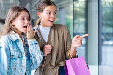 Alışveriş torbaları tutan ve vitrinlere bakan iki mutlu beyaz kadın. Şehirde alışveriş ve arkadaşlığın olduğu bir günde samimi ve neşeli bir şehir anı. 