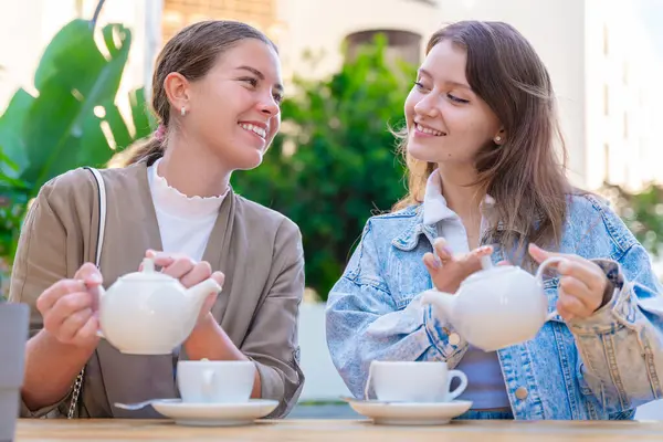 İki beyaz kadın açık hava kafeteryasında oturmuş birbirlerine gülümseyip çay doldururken güneşli bir günde rahat ve keyifli bir dostluk, sohbet ve keyif dolu bir anın tadını çıkarıyorlar.. 