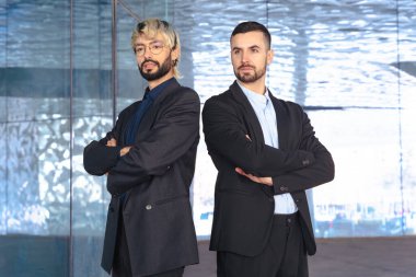 Çapraz kollu takım elbiseli iki kendine güvenen profesyonel erkek modern bir ofisin içinde kameraya karşı ciddidir. Şirket başarısı, takım çalışması ve iş ortamında liderlik.. 