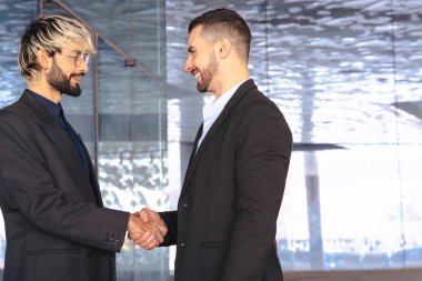 Modern cam bir ofiste takım elbiseli iki profesyonel işadamı el sıkışıyor. İş anlaşması, anlaşma ya da modern tasarım ile kurumsal bir iç mekanda ortaklık. Boşluğu kopyala