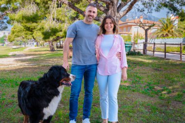 Gülümseyen çift, güneşli bir günde yeşil bir parkta büyük köpekleriyle poz veriyor. Aşk, arkadaşlık, yaşam tarzı, evcil hayvan bakımı ve açık havada yaşam gibi konular için ideal bir ortam.. 