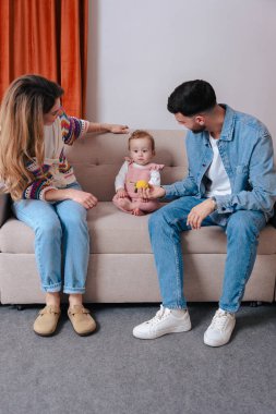 Gülümseyen ebeveynler koltukta otururken oyuncak tutan kızlarıyla oyun oynamaktan hoşlanırlar. Sıcak bir yuva ortamında sevgi, renk ve sıcaklıkla dolu neşeli bir aile bağlılık anı.. 