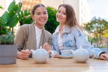 Dışarıda çay içerken gülümseyen ve kameraya bakan iki beyaz kadın portresi. Şehirde güneşli bir günde rahat ve neşeli bir arkadaşlık, rahatlık ve sohbet anı.. 