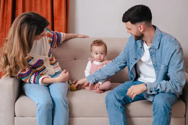 Küçük kızlarıyla oyuncak bir topla oynarken koltukta oturan gülümseyen ebeveynler. Aşk, aile bağları, erken gelişim ve ebeveynlik gibi konular için ideal ev ortamları. 