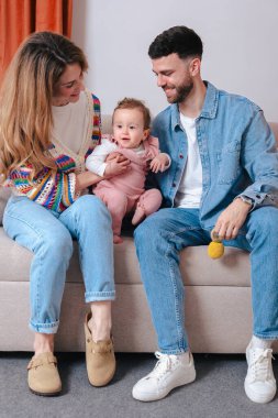 Gülümseyen ebeveynler koltukta otururken oyuncak tutan kızlarıyla oyun oynamaktan hoşlanırlar. Sıcak bir yuva ortamında sevgi, renk ve sıcaklıkla dolu neşeli bir aile bağlılık anı.. 