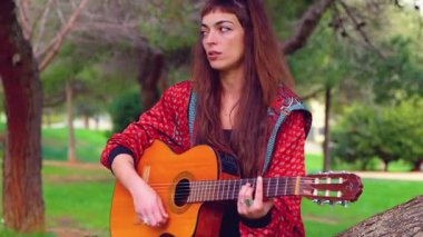 Genç bayan müzisyen, sakin bir açık hava parkında akustik gitarla şarkı söylüyor. Doğa tarafından çevrelenmiş, tutku, yaratıcılık ve duyguyu gündelik bir ortamda müzik yoluyla ifade eder.. 