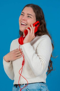 Kırmızı bir akıllı telefondan konuşan neşeli genç bir kadının dikey görüntüsü. Elini göğsüne koyup gülüyor. Parlak mavi bir arka plana yaslanıyor. Sıradan bir anda.. 