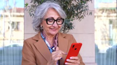 Gri saçlı, gözlüklü, elinde kırmızı bir telefon tutan düşünceli bir son sınıf öğrencisi. Mesajı düşünürken çenesine dokunuyor. Dijital okuryazarlığı, karar verme yetisini ve bağlantıyı yansıtıyor.. 