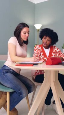 İki kadın ahşap bir masada iş birliği yapıyor, ev içi, kıyafet, takım çalışması, konsantrasyon, yaratıcı proje, arkadaşlık, modern daire, dikey görüntü biçimi üzerine odaklanıyorlar. 