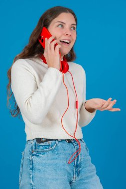 Kırmızı bir akıllı telefondan konuşan neşeli genç bir kadının dikey görüntüsü. Elini göğsüne koyup gülüyor. Parlak mavi bir arka plana yaslanıyor. Sıradan bir anda.. 
