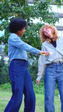 Parkta birlikte dans eden, gülümseyen ve eğlenen iki neşeli genç kadın çevrenin yeşillik ve rahat bir atmosferle çevrili olduğu neşeli ve eğlenceli bir anın tadını çıkarıyorlar. 