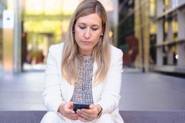 Bej ceketli neşeli bir adamın portresi gülümserken kırmızı bir akıllı telefonu canlı mavi arka plan, teknoloji, iletişim ve modern yaşam tarzını dikey biçimde kullanıyordu.