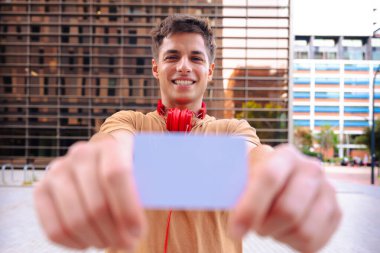 Boynunda kırmızı kulaklıklarla gülümseyen genç bir adamın portresi ön planda bir kart gösteriyor, bulanık bir şehir geçmişi var, pozitif ve modern bir tavır sergiliyor.. 