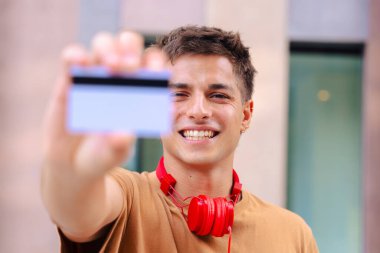 Boynunda kırmızı kulaklıklarla gülümseyen genç bir adamın portresi ön planda bir kart gösteriyor, bulanık bir şehir geçmişi var, pozitif ve modern bir tavır sergiliyor.. 