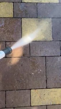 Çakıl taşlarını yıkıyor. Toprak farklı yönlere uçar. Gündüz vakti. Paving Stones Pavement 'i yüksek basınçlı çamaşır makinesiyle temizlemek, kaldırım taşlarını su jetiyle yıkamak. Sting temizlik konsepti. sstkVertical