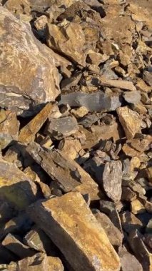 Farklı boyutlarda ve şekillerde kaotik bir şekilde üst üste duran taşlar kümesi. Taşların düz olmayan bir yüzeyi var ve güneş ışığı üzerlerinde parlıyor. Yerel bir dağ ya da taş ocağı. Yüksek kalite 4k