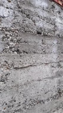 Sert ve pürüzlü deseni olan beton bir duvar. Betonun yapısı büyük boşluklar, açıkta kalan çakıllar ve bütünlük kaybı ile dengesizdir. Yüzeyin katmanlı bir görünüşü var. Yüksek kalite
