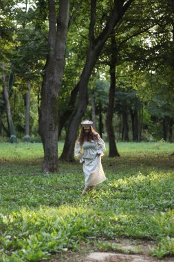 Uzun açık renk elbiseli bir kız ormanda çimlerin üzerinde yalınayak yürüyor. Kafasında bir bere var, saçları gevşek. Kız yere bakıyor. Doğayla birlik, huzur ve aydınlık. Zihinsel denge. Yüksek