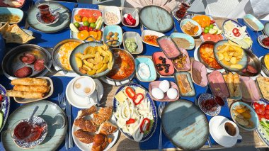 Türk kahvaltısı dışarıda servis ediliyor. Masada birçok tabak var - yumurta, zeytin, sosis, patates, hamur işi, meyve ve geleneksel çay bardaklarda ve kahvede. yemek konsepti fotoğrafı.